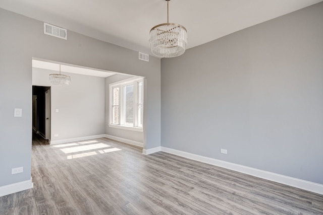 empty room with baseboards, a notable chandelier, wood finished floors, and visible vents