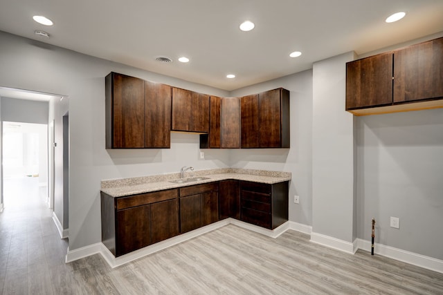 kitchen with baseboards, a sink, light wood finished floors, and dark brown cabinets