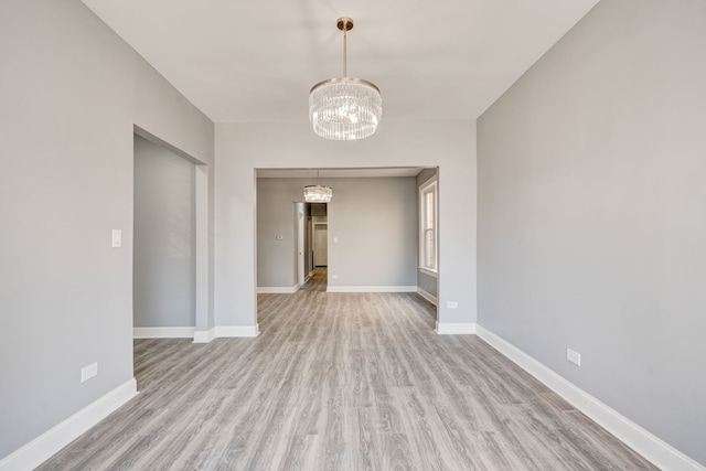 empty room featuring an inviting chandelier, baseboards, and wood finished floors