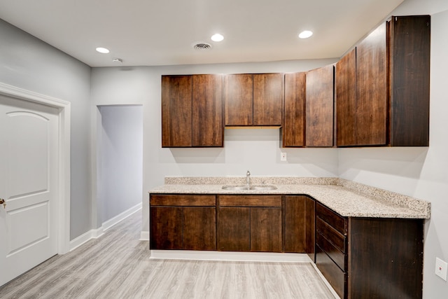 kitchen with dark brown cabinetry, a sink, baseboards, light wood-type flooring, and visible vents