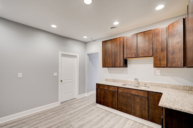 kitchen with light stone countertops, a sink, light wood finished floors, baseboards, and visible vents