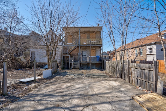 back of property featuring fence, stairs, a balcony, and brick siding