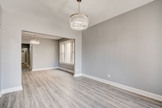 spare room featuring baseboards, a chandelier, and wood finished floors