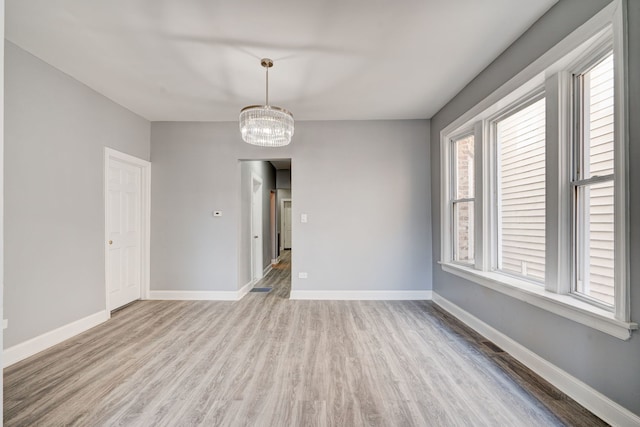unfurnished room with baseboards, an inviting chandelier, a wealth of natural light, and wood finished floors