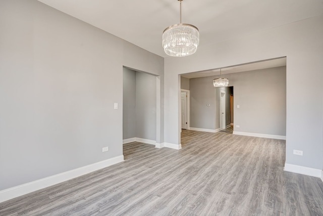 spare room featuring baseboards, wood finished floors, and a notable chandelier