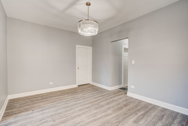 empty room featuring baseboards, light wood-type flooring, and a notable chandelier