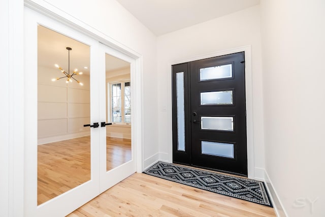 foyer entrance featuring baseboards, french doors, wood finished floors, and a notable chandelier