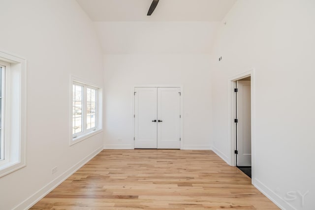 unfurnished bedroom featuring baseboards, a ceiling fan, light wood-style floors, and high vaulted ceiling