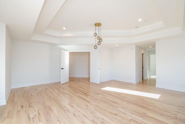 unfurnished room featuring a raised ceiling, baseboards, light wood finished floors, ornamental molding, and recessed lighting