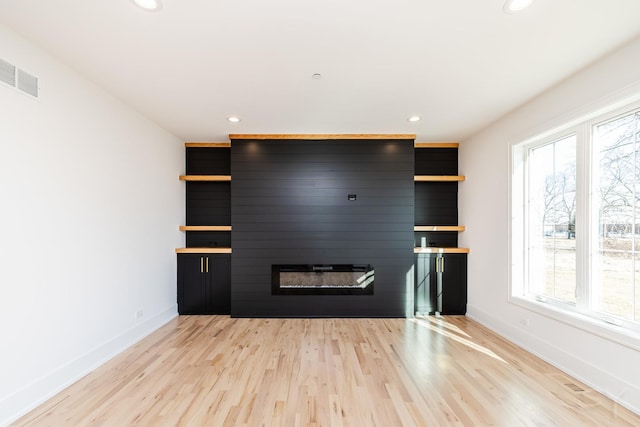 unfurnished living room with a large fireplace, baseboards, light wood finished floors, and a wealth of natural light