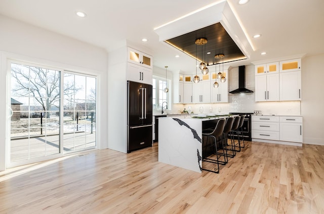 kitchen featuring wall chimney range hood, light wood-style floors, a breakfast bar area, tasteful backsplash, and black appliances