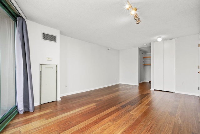 unfurnished living room with a textured ceiling, visible vents, baseboards, and hardwood / wood-style floors