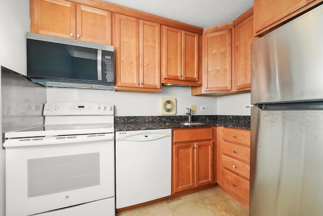 kitchen featuring brown cabinets, a sink, a textured ceiling, dark stone countertops, and stainless steel appliances
