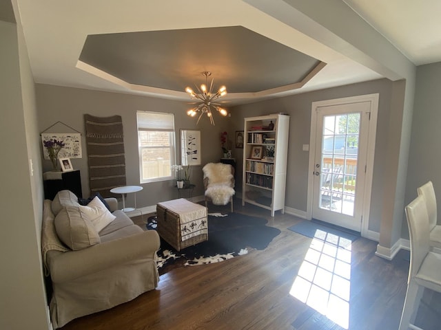 living area featuring a raised ceiling, baseboards, wood finished floors, and a notable chandelier