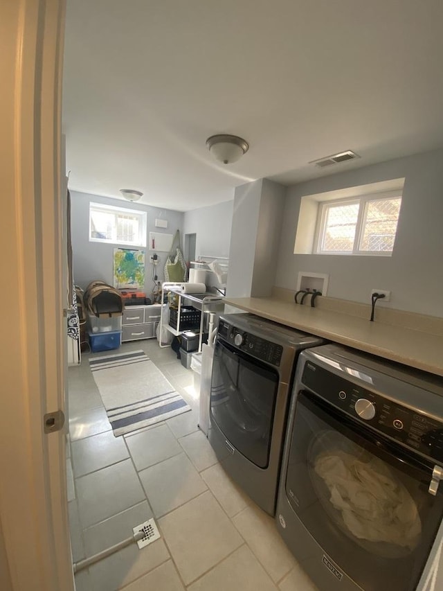 washroom with light tile patterned floors, laundry area, washing machine and dryer, and visible vents
