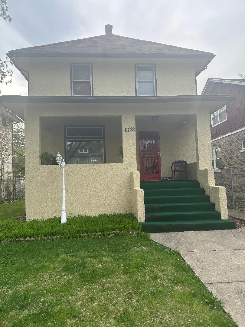 american foursquare style home with stucco siding, covered porch, a front yard, and fence
