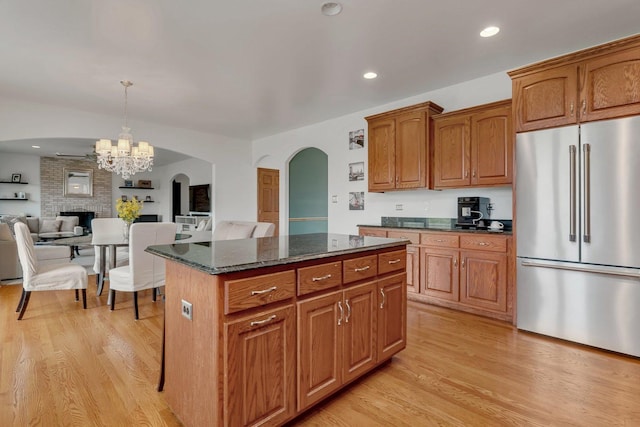 kitchen featuring freestanding refrigerator, a center island, dark stone counters, arched walkways, and light wood-style flooring