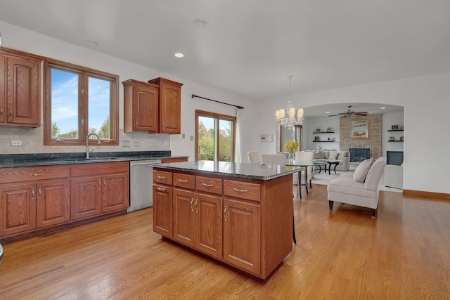kitchen with stainless steel dishwasher, backsplash, light wood-style flooring, and a brick fireplace