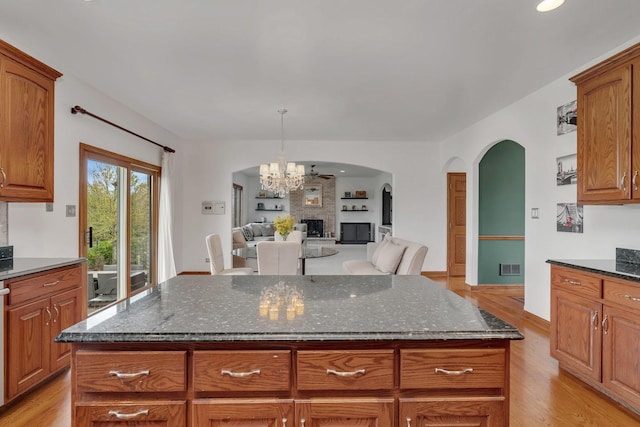 kitchen featuring visible vents, arched walkways, dark stone countertops, a notable chandelier, and light wood-style floors