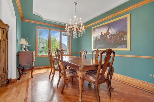 dining area with baseboards, ornamental molding, wood finished floors, and a chandelier