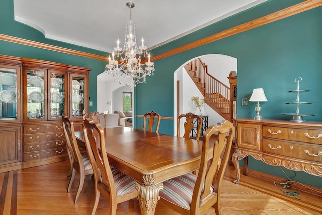 dining area with an inviting chandelier, arched walkways, wood finished floors, ornamental molding, and stairway