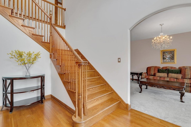 stairs featuring arched walkways, baseboards, an inviting chandelier, and wood finished floors