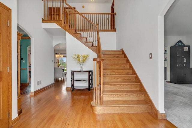 stairway with visible vents, arched walkways, a towering ceiling, and wood finished floors