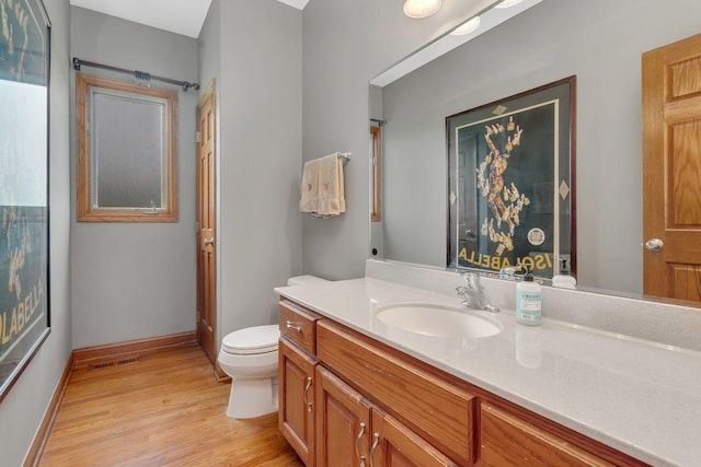 bathroom with vanity, toilet, baseboards, wood finished floors, and visible vents