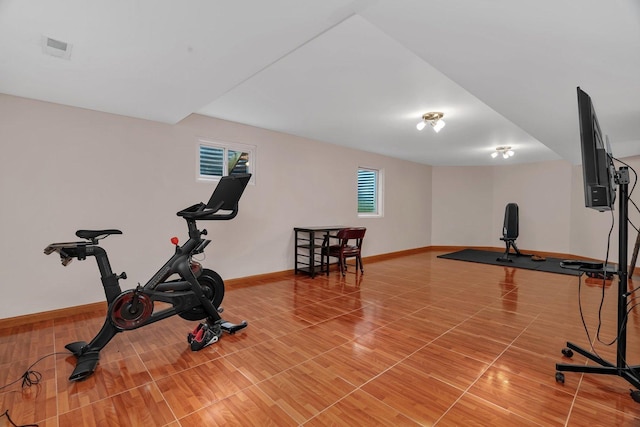 exercise area with baseboards, light wood finished floors, and visible vents