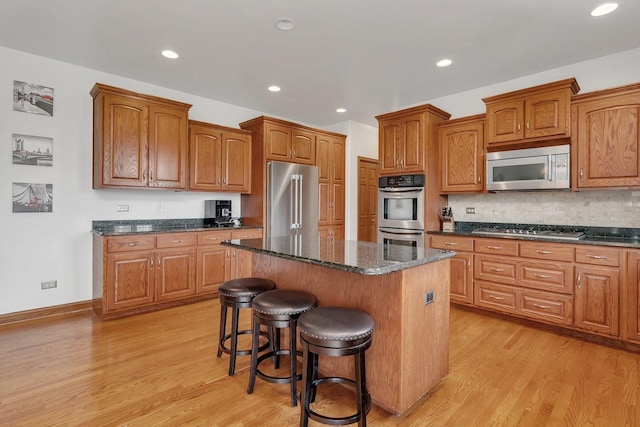 kitchen featuring a breakfast bar area, a kitchen island, appliances with stainless steel finishes, dark stone countertops, and light wood-style floors