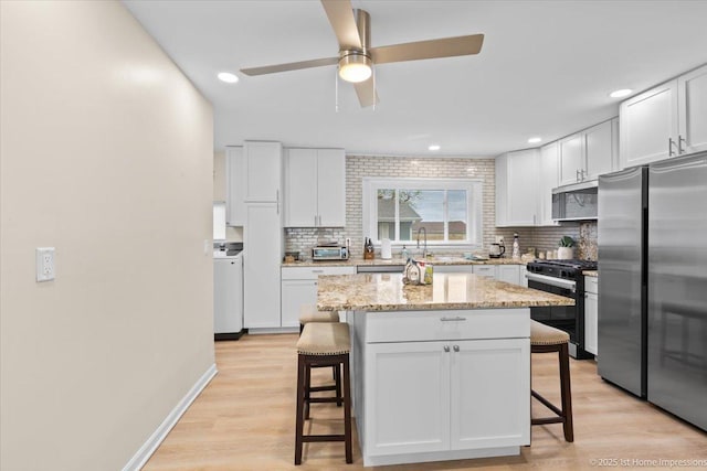 kitchen featuring a breakfast bar area, stainless steel appliances, a ceiling fan, and backsplash
