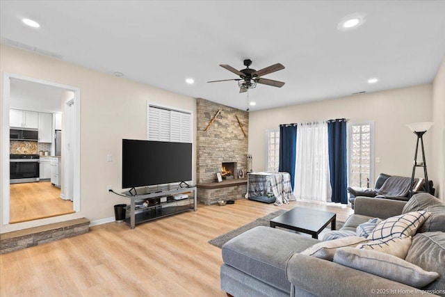 living room with recessed lighting, ceiling fan, a stone fireplace, and light wood-type flooring