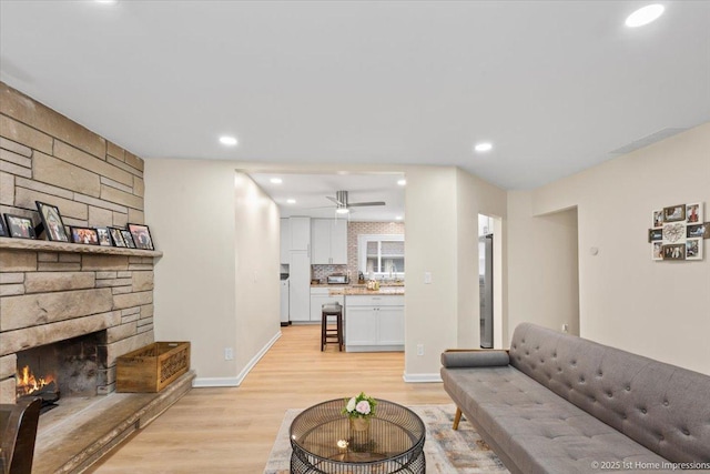 living area featuring a fireplace, baseboards, light wood-type flooring, recessed lighting, and a ceiling fan