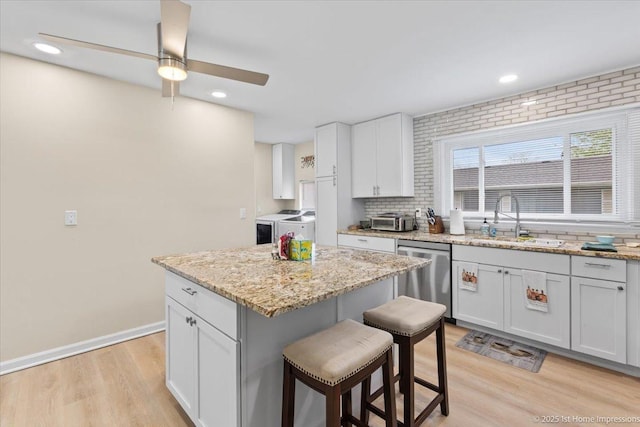 kitchen with a kitchen breakfast bar, ceiling fan, washing machine and clothes dryer, stainless steel dishwasher, and a sink