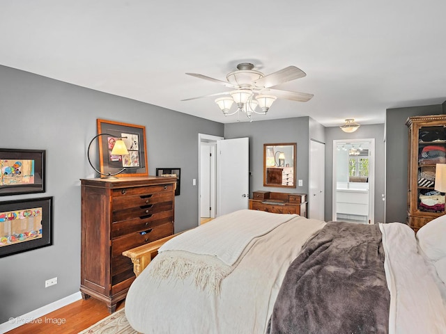 bedroom with ensuite bath, wood finished floors, baseboards, and ceiling fan