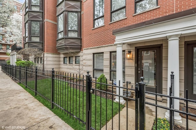 view of exterior entry featuring a yard, brick siding, and fence