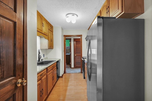 kitchen with light wood-type flooring, dishwasher, a sink, light countertops, and freestanding refrigerator