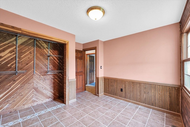 unfurnished bedroom with a wainscoted wall, multiple windows, a textured ceiling, and light tile patterned flooring
