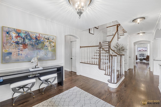 foyer entrance with arched walkways, crown molding, stairs, wood finished floors, and baseboards