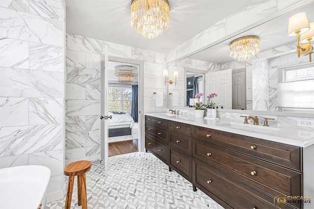 ensuite bathroom with a chandelier, a freestanding tub, double vanity, and tile walls