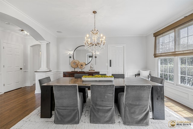 dining space with arched walkways, wood finished floors, ornate columns, a wainscoted wall, and a chandelier