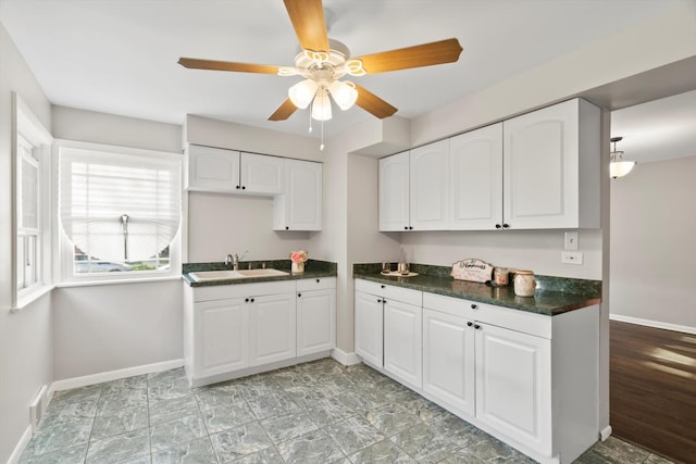 kitchen featuring a sink, baseboards, dark countertops, and white cabinetry