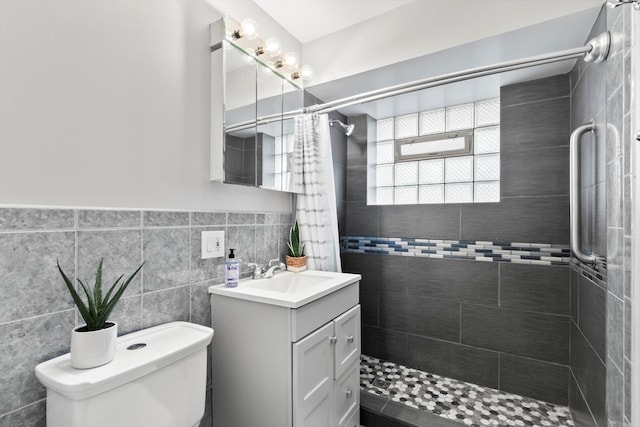 full bath with tile walls, a tile shower, vanity, a wainscoted wall, and toilet