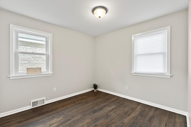 spare room featuring baseboards, dark wood finished floors, and visible vents