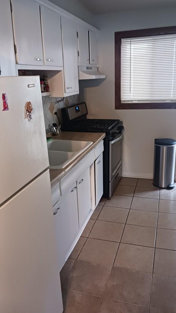 7019 N Ridge Blvd Unit 3B, Chicago, IL 60645 - kitchen featuring freestanding refrigerator, stainless steel range with gas cooktop, under cabinet range hood, light tile patterned floors, and white cabinetry
