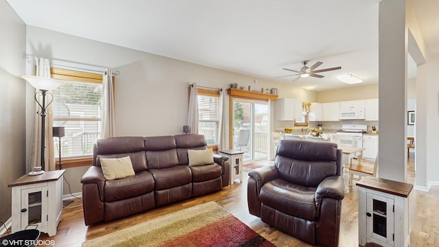 living room featuring ceiling fan, baseboards, and light wood finished floors