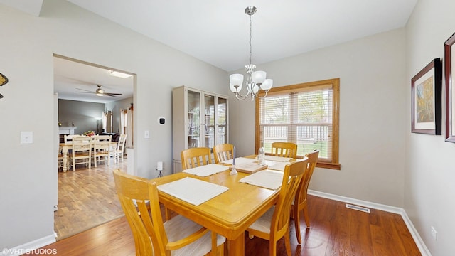 dining area with ceiling fan with notable chandelier, baseboards, visible vents, and wood finished floors