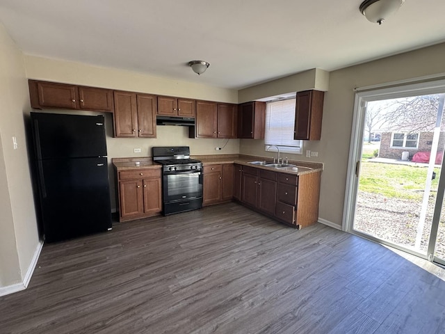 kitchen featuring dark wood-style flooring, a sink, baseboards, black appliances, and under cabinet range hood