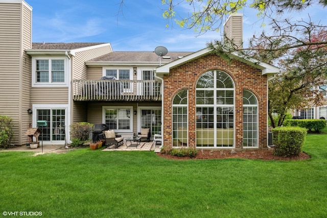 rear view of property with a chimney, brick siding, a balcony, a yard, and a patio