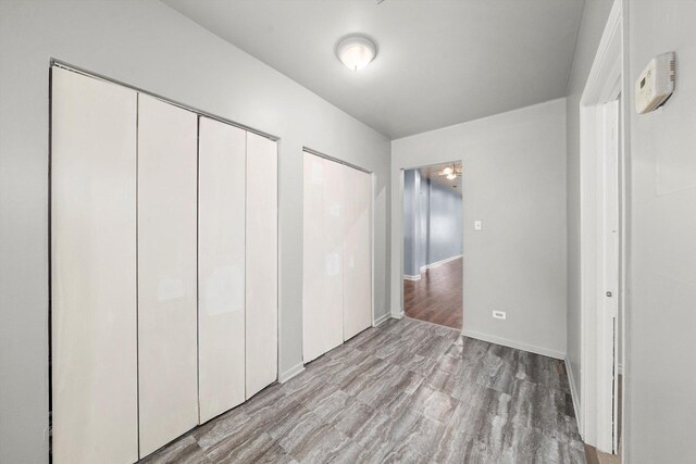unfurnished bedroom with baseboards, multiple closets, and wood finished floors